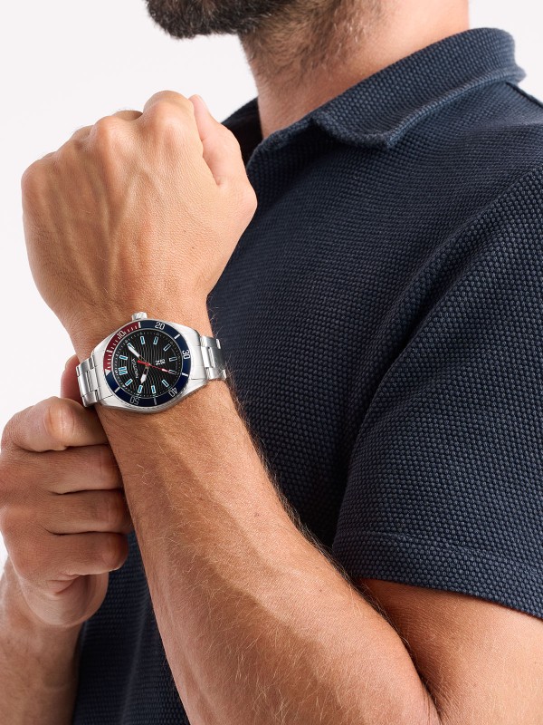 NAPFWS503: NAUTICA Finn World sat sa crnim brojčanikom, čeličnom narukvicom i plavo-crvenim top ringom. Sportski stil, 100m vodootporan, kvarcni mehanizam.