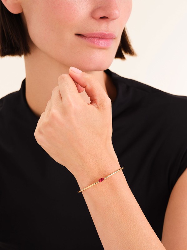 Rosefield JBRMG-J1243 – elegantna ženska narukvica od nerđajućeg čelika sa otvorenim krajevima u boji žutog zlata, ukrašena crvenim cirkonom. Veličina: 6 cm x 5 cm. Luksuzan komad koji unosi toplinu i sofisticiranost u svaki stil.