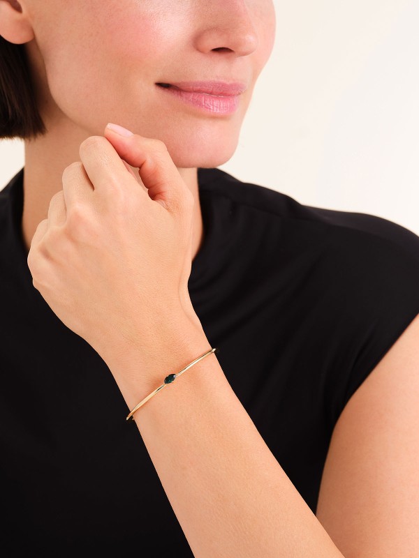 Rosefield JBEMG-J1242 – sofisticirana ženska narukvica od nerđajućeg čelika sa otvorenim krajevima u boji žutog zlata, ukrašena zelenim cirkonom. Veličina: 6 cm x 5 cm. Savršen dodatak za elegantan i prefinjen stil.