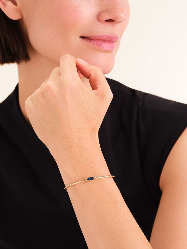 Rosefield JBMMG-J1241 – elegantna ženska narukvica od nerđajućeg čelika sa otvorenim krajevima u boji žutog zlata, ukrašena plavim cirkonom. Veličina: 6 cm x 5 cm. Idealna kombinacija elegancije i modernog dizajna.