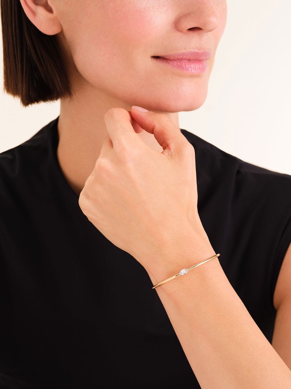 Rosefield JBCMG-J1240 – elegantna ženska narukvica od nerđajućeg čelika sa otvorenim krajevima u boji žutog zlata, ukrašena belim cirkonom. Veličina: 6 cm x 5 cm. Savršen spoj minimalizma i luksuza.