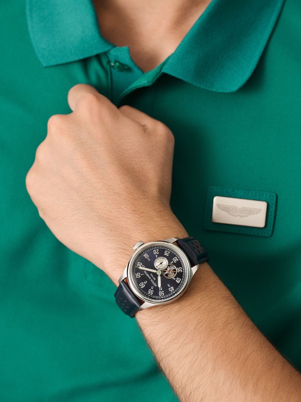 Aston Martin MTTS1F502 – luksuzni automatik sat koji kombinuje eleganciju i tehničku preciznost. Kućište od nerđajućeg čelika prečnika 41mm sadrži skeleton brojčanik u teget boji sa istorijskim logom Aston Martina iz 1913. godine. Transparentna poleđina otkriva automatski mehanizam sa rotorom u prepoznatljivoj podium zelenoj boji. Uparen sa teget kožnom narukvicom, ovaj model spaja britansku sofisticiranost i savremeni dizajn za istinske poznavaoce stila.