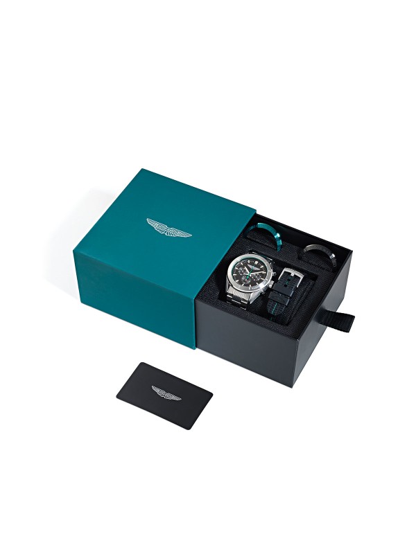 Aston Martin MTIB1F501 – ekskluzivni muški box set hronograf sa tri zamenljiva top ringa (srebrni, crni i podium zeleni) i dve narukvice – čeličnom i silikonskom. Kućište od recikliranog čelika, crni teksturirani brojčanik i osvetljene kazaljke odražavaju sportski luksuz i preciznost Aston Martin dizajna.