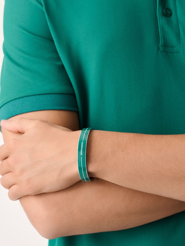 Aston Martin MJITF5BM1 – muška čvrsta narukvica od nerđajućeg čelika 316L u boji srebra, ukrašena podium zelenim emajlom, belom linijom i ugraviranim natpisom ASTON MARTIN. Simbol elegancije, performansi i britanskog luksuza. Dimenzije (veličina M): 65 mm x 50 mm.
