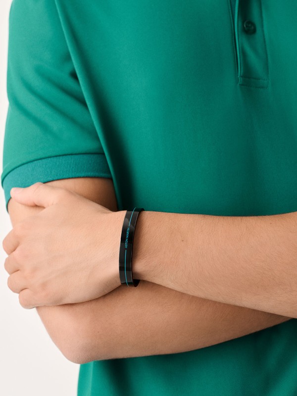 Aston Martin MJITF5BM0 – muška čvrsta narukvica od nerđajućeg čelika 316L u gun metal boji, ukrašena crnim emajlom i plavom linijom. Ugraviran natpis ASTON MARTIN naglašava prefinjen sportski stil. Simbol luksuza i britanske elegancije. Dimenzije (veličina M): 65 mm x 50 mm.