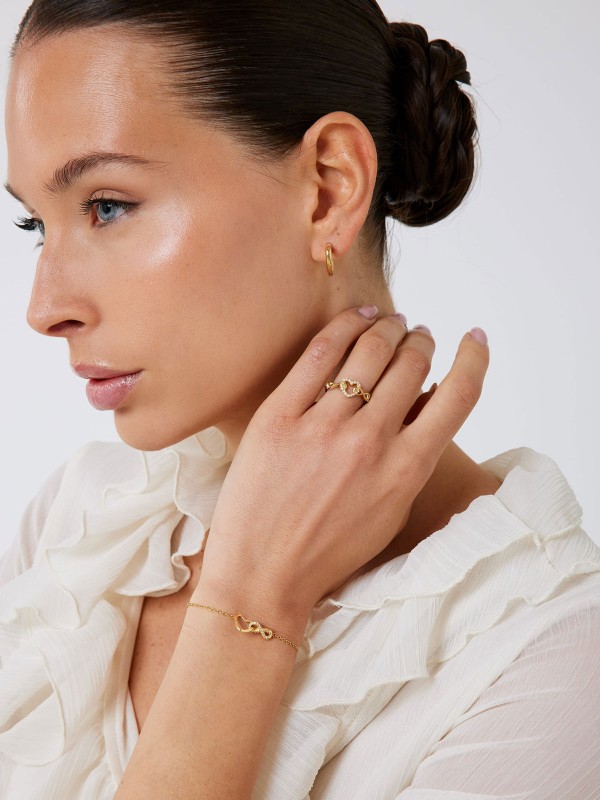 Guess ICONIQUE prsten od nerđajućeg čelika u boji žutog zlata, ukrašen motivom beskonačnosti i srca. Moderan i romantičan detalj. Veličina 54.