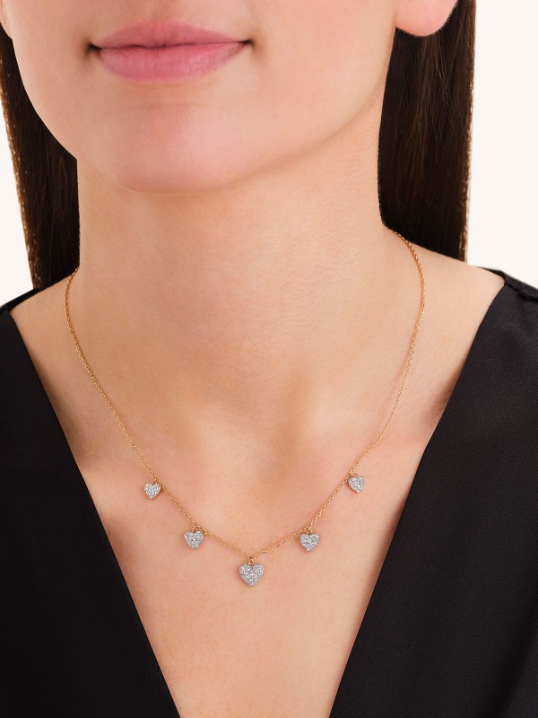 Ogrlica u zlatnom tonu sa nizom visećih srca. Ukrašena belim cirkonima za razigran i svetlucav efekat oko vrata.